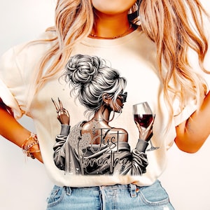 Peut inclure: Un t-shirt blanc avec un motif repr&eacute;sentant une femme tenant un verre de vin rouge et le texte "Just Breathe".