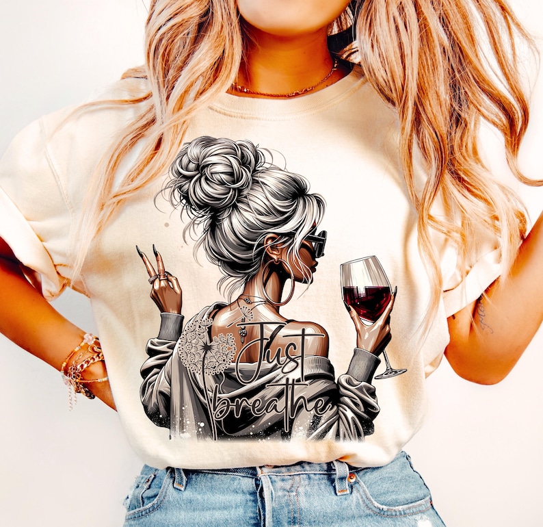 Peut inclure: Un t-shirt blanc avec un motif repr&eacute;sentant une femme tenant un verre de vin rouge et le texte "Just Breathe".