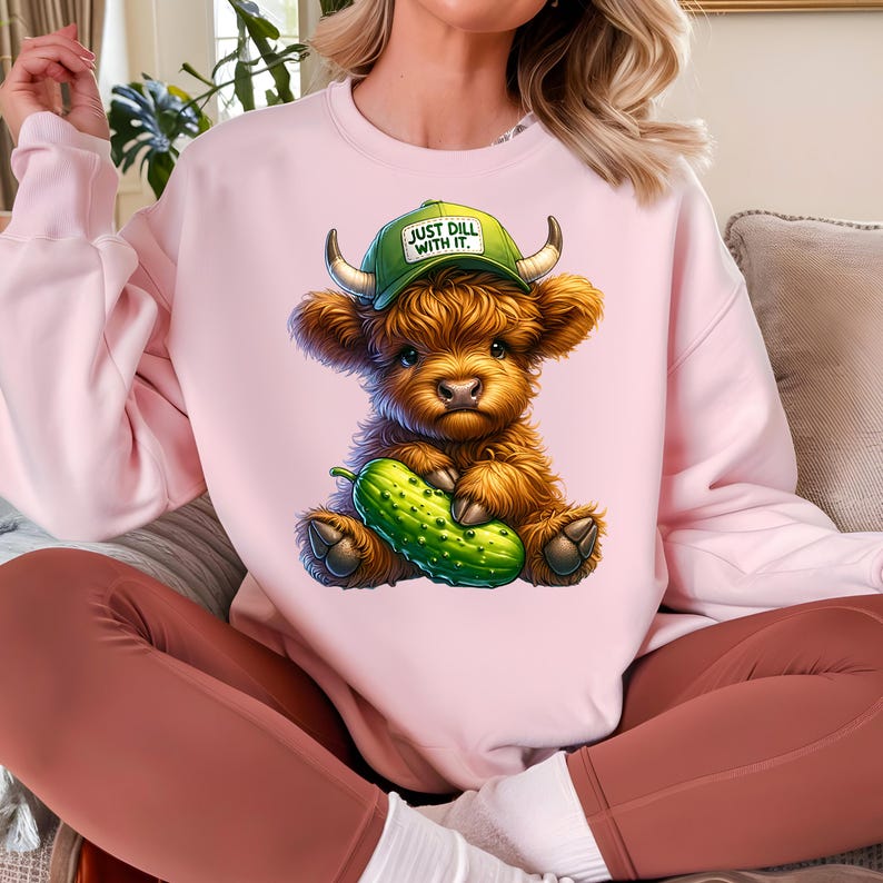 May include: A pink sweatshirt with a cartoon highland cow wearing a green hat that says "Just Dill With It." The cow is holding a green pickle.