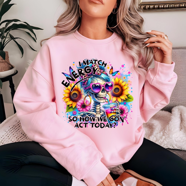 May include: Pink sweatshirt with a colorful graphic of a skeleton wearing sunglasses and holding a drink. The graphic includes the text "I Match Energy So How We Gon' Act Today?"
