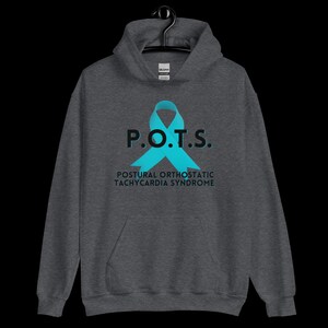 Pode incluir: Um moletom cinza escuro com o texto "P.O.T.S." e o nome completo da condi&ccedil;&atilde;o, "Postural Orthostatic Tachycardia Syndrome". Uma fita azul-turquesa &eacute; exibida. O moletom com capuz est&aacute; pendurado em um cabide preto.