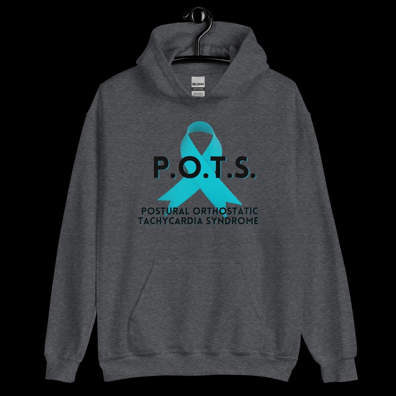 Pode incluir: Um moletom cinza escuro com o texto "P.O.T.S." e o nome completo da condi&ccedil;&atilde;o, "Postural Orthostatic Tachycardia Syndrome". Uma fita azul-turquesa &eacute; exibida. O moletom com capuz est&aacute; pendurado em um cabide preto.