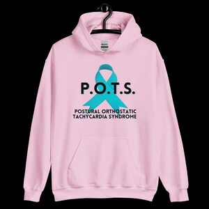 Pode incluir: Moletom rosa claro com um la&ccedil;o turquesa e o texto "P.O.T.S." acima de "Postural Orthostatic Tachycardia Syndrome" em preto. O moletom tem um bolso frontal e um capuz com cord&atilde;o.