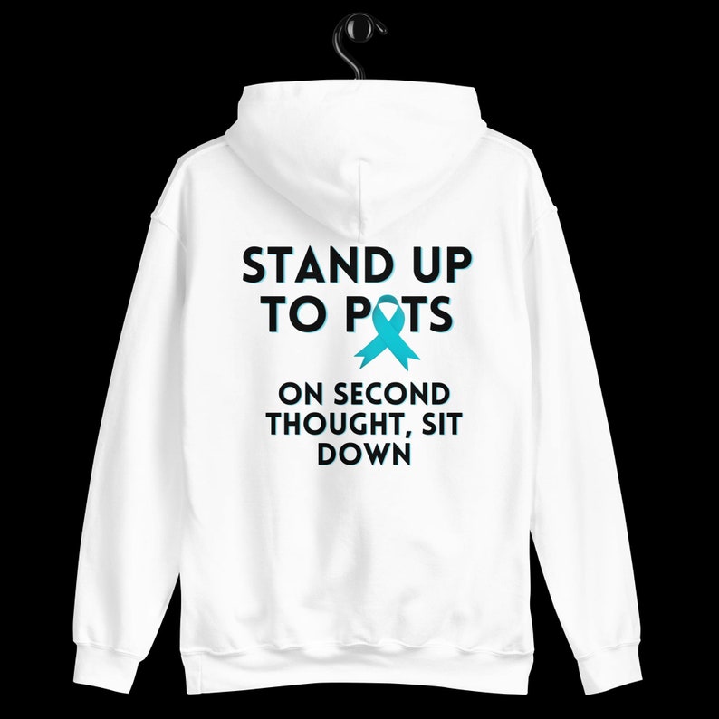 Pode incluir: Moletom branco com a frase "STAND UP TO POTS" acima de uma fita azul-petr&oacute;leo e a frase "ON SECOND THOUGHT, SIT DOWN". O moletom est&aacute; pendurado em um cabide preto em um fundo preto.