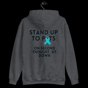 Pode incluir: Moletom cinza escuro com o texto "STAND UP TO POTS" acima de uma fita azul-turquesa e o texto "ON SECOND THOUGHT, SIT DOWN". O moletom est&aacute; pendurado em um cabide preto.