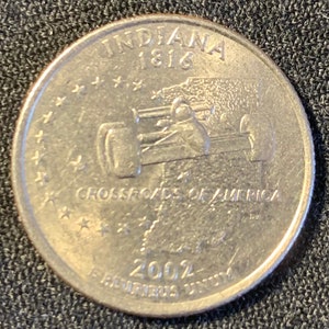 Może przedstawiać: Srebrna amerykańska moneta o wartości ćwierć dolara przedstawiająca samochód wyścigowy i tekst "Indiana 1816 Crossroads of America 2002 E Pluribus Unum".