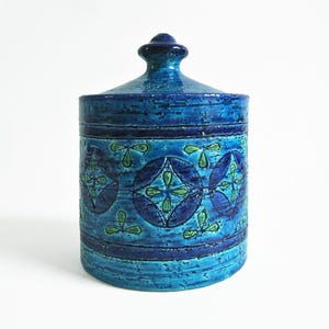 Puede incluir: Un tarro de cerámica azul y verde con tapa. El tarro tiene un patrón geométrico con flores azules y verdes.
