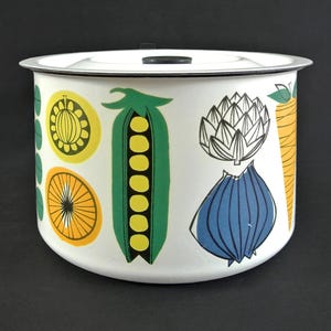 May include: White enamelware container with a lid, decorated with colorful illustrations of vegetables. The design includes a green pea pod, orange slices, and a blue onion. The container has a black handle on the lid.