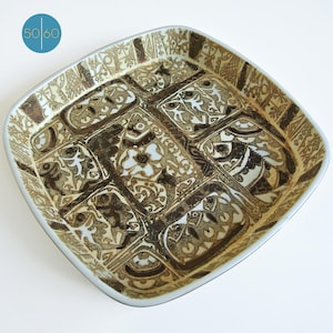 May include: A square ceramic serving dish with a white background and a brown and black geometric pattern. The pattern features stylized flowers and abstract shapes.