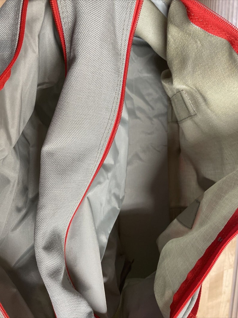 Puede incluir: El interior de una bolsa de mano con cremallera gris y roja. La bolsa est&aacute; hecha de un tejido suave y tejido. La cremallera es roja y recorre la parte superior de la bolsa.