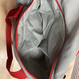 Puede incluir: Una bolsa de lona gris y roja con cierre de cremallera. La bolsa est&aacute; abierta y el interior es visible.