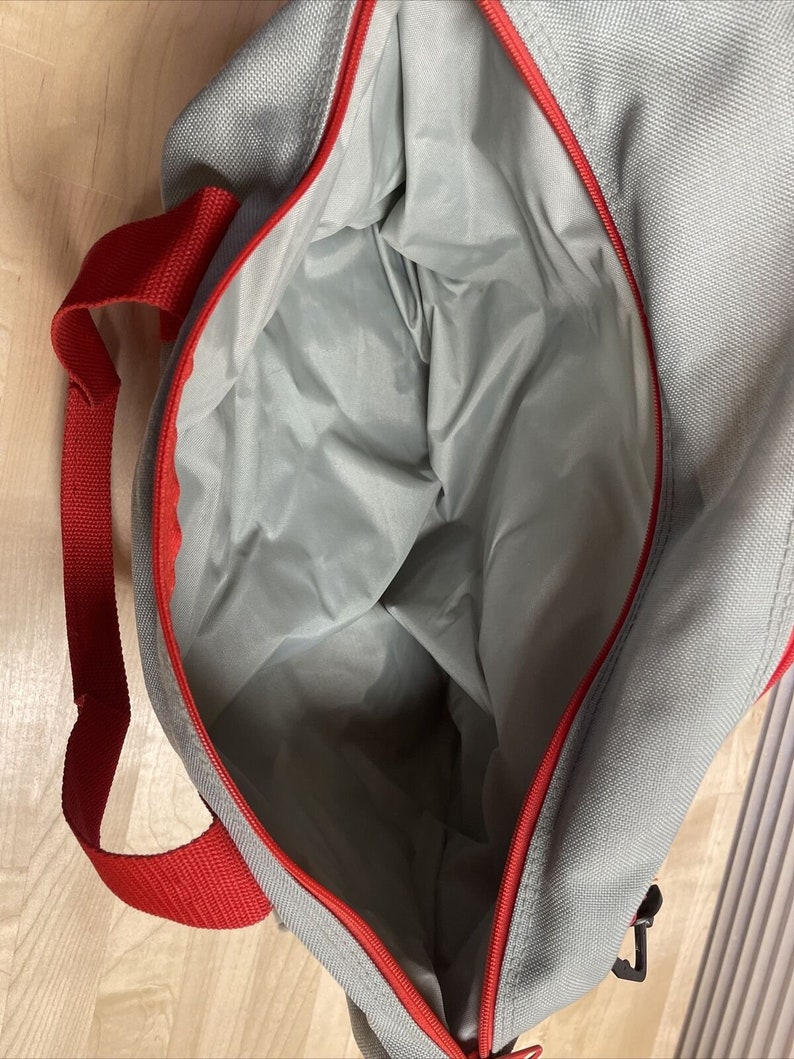 Puede incluir: Una bolsa de lona gris y roja con cierre de cremallera. La bolsa est&aacute; abierta y el interior es visible.