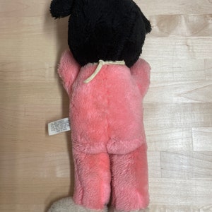 Peut inclure: Jouet en peluche rose avec des cheveux noirs en queue de cheval. Le jouet porte un pyjama rose avec des pieds blancs. Le jouet a une &eacute;tiquette qui indique "Tous nouveaux mat&eacute;riaux. Ext&eacute;rieur : 100 % polyester. Remplissage : 100 % polyester. Entretien : Lavage en surface uniquement. Fabriqu&eacute; en Chine."