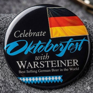 May include: A round black pin-back button featuring the German flag in the upper right corner. The text reads Celebrate Oktoberfest with WARSTEINER Best Selling German Beer in the World, with a blue and white diamond pattern along the bottom edge.