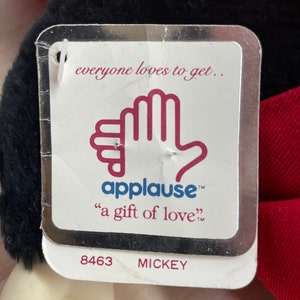 May include: A white tag with a silver border and the text "everyone loves to get... applause&trade; "a gift of love&trade;" 8463 MICKEY"  The tag features a red hand with the word "applause" in red text.