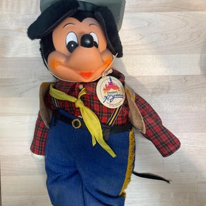 Pu&ograve; includere: Bambola di peluche vintage di Topolino con camicia a quadri, jeans blu e stivali da cowboy. La bambola ha un cappello grigio e una sciarpa gialla. &Egrave; presente un'etichetta del 30&deg; anniversario di Disneyland.