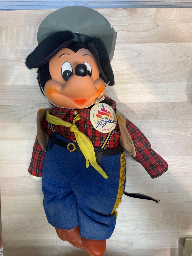Pu&ograve; includere: Bambola di peluche vintage di Topolino con camicia a quadri, jeans blu e stivali da cowboy. La bambola ha un cappello grigio e una sciarpa gialla. &Egrave; presente un'etichetta del 30&deg; anniversario di Disneyland.