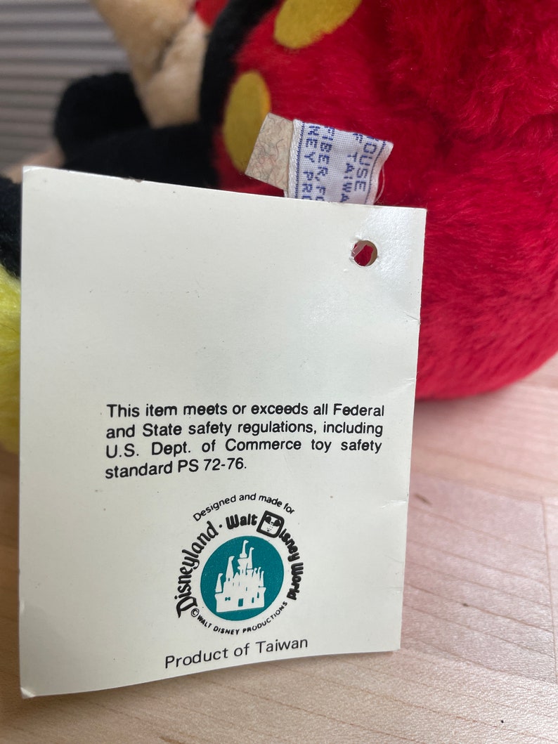 May include: A white tag with black text that reads "This item meets or exceeds all Federal and State safety regulations, including U.S. Dept. of Commerce toy safety standard PS 72-76. Designed and made for Walt Disney World. WALT DISNEY PRODUCTIONS. Product of Taiwan."