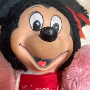 Peut inclure: Un jouet en peluche de Minnie Mouse portant une robe rose et rouge avec le mot "Minnie" brod&eacute; sur le devant.
