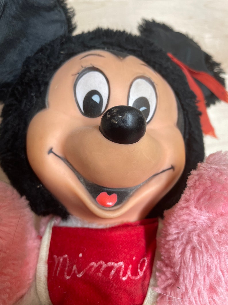Peut inclure: Un jouet en peluche de Minnie Mouse portant une robe rose et rouge avec le mot "Minnie" brod&eacute; sur le devant.