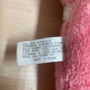 Peut inclure: Une &eacute;tiquette blanche avec du texte noir attach&eacute;e &agrave; un jouet en peluche rose. L'&eacute;tiquette indique "All New Materials Contents: Synthetic Fiber Walt Disney Distributing Co Lake Buena Vista, Fla. 3283 Licensed in Penn. 268, Ohio 84 Mass. 214, Maine 103 Made in Korea."
