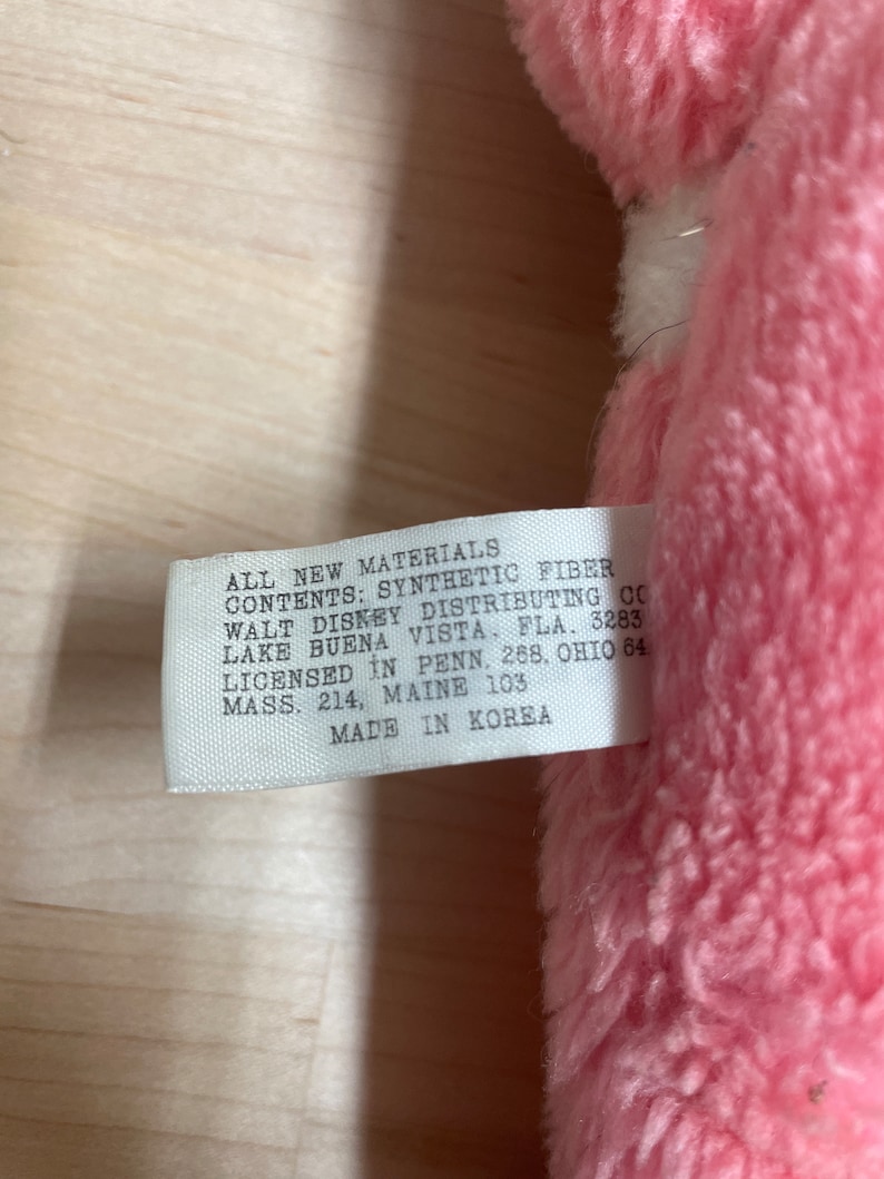 Peut inclure: Une &eacute;tiquette blanche avec du texte noir attach&eacute;e &agrave; un jouet en peluche rose. L'&eacute;tiquette indique "All New Materials Contents: Synthetic Fiber Walt Disney Distributing Co Lake Buena Vista, Fla. 3283 Licensed in Penn. 268, Ohio 84 Mass. 214, Maine 103 Made in Korea."