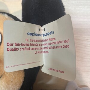May include: A Mickey Mouse puppet with a black head and tan face. The puppet has a tag that reads "applause puppets" and "Hi, my name is Mickey Mouse." The tag also includes the text "Quality crafted puppets designed with an extra dose of playfulness."