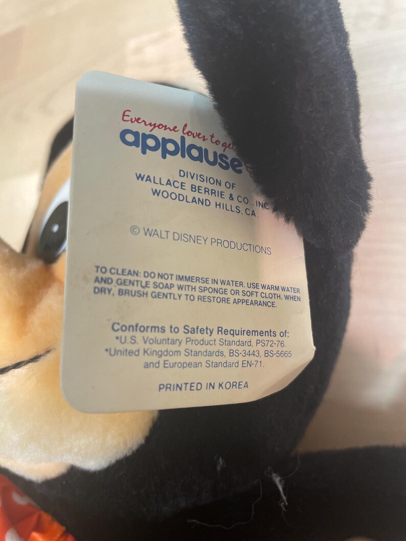 May include: A plush toy with a black ear and a tag that reads "Everyone loves to get applause." The tag also includes the text "WALT DISNEY PRODUCTIONS" and "PRINTED IN KOREA."