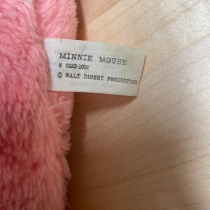 Peut inclure: Une &eacute;tiquette blanche avec du texte noir qui indique "Minnie Mouse # 0223-1002 &copy; WALT DISNEY PRODUCTIONS" attach&eacute;e &agrave; un jouet en peluche rose.