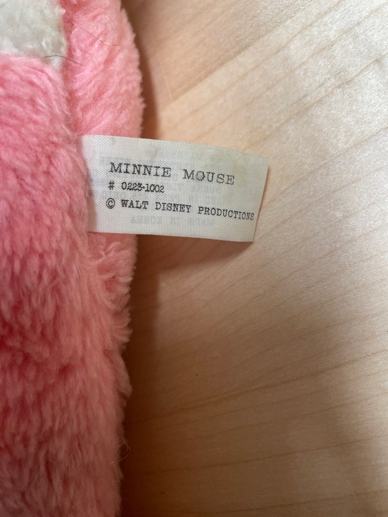Peut inclure: Une &eacute;tiquette blanche avec du texte noir qui indique "Minnie Mouse # 0223-1002 &copy; WALT DISNEY PRODUCTIONS" attach&eacute;e &agrave; un jouet en peluche rose.