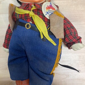 Pu&ograve; includere: Bambola vintage di Topolino con camicia a quadri rossa, jeans blu e gilet marrone. La bambola ha un cravattino giallo e un'etichetta del 30&deg; anniversario di Disneyland. La bambola indossa stivali arancioni.