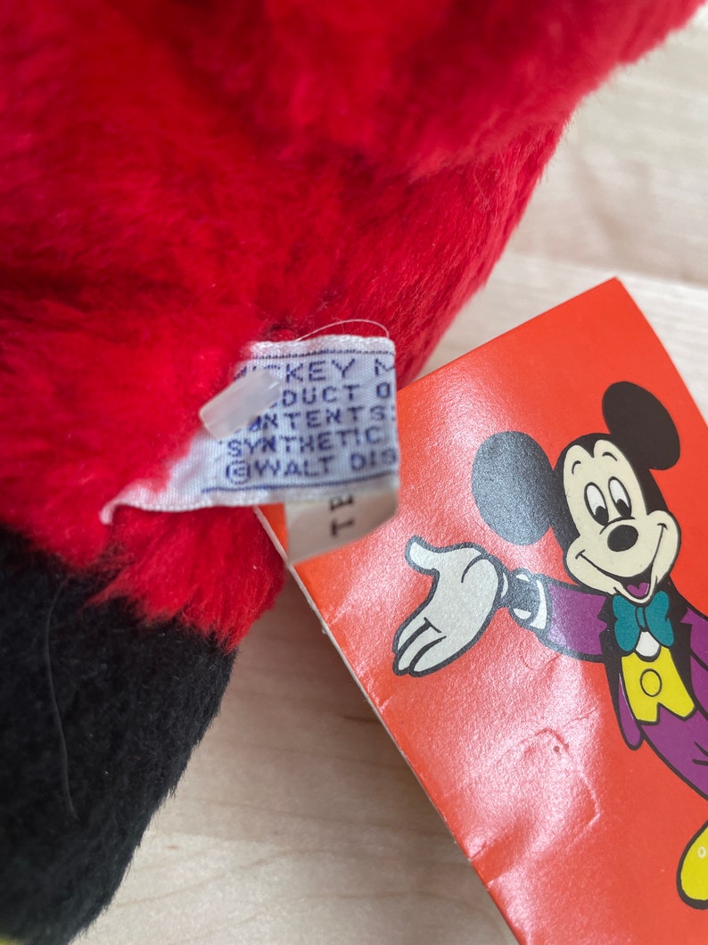 May include: Red and black plush Mickey Mouse toy with a tag that reads "Mickey Mouse Product of All Contents Synthetic Fibre Walt Disney Productions."