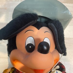 Pu&ograve; includere: Bambola di peluche vintage di Topolino con cappello e orecchie neri, camicia a quadri rossi e gilet giallo. La bambola ha un naso rotondo nero, occhi bianchi e un'etichetta con il logo Disneyland.