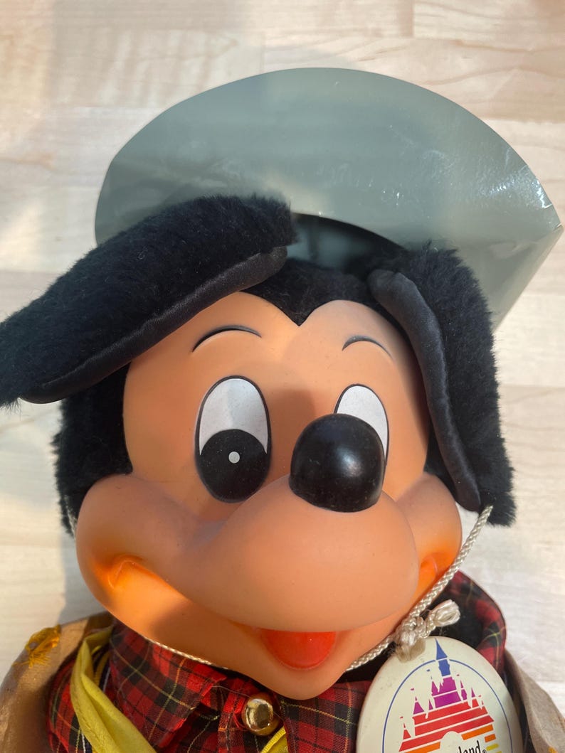 Pu&ograve; includere: Bambola di peluche vintage di Topolino con cappello e orecchie neri, camicia a quadri rossi e gilet giallo. La bambola ha un naso rotondo nero, occhi bianchi e un'etichetta con il logo Disneyland.