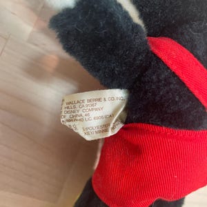 Może przedstawiać: Pluszowa lalka Myszki Miki z czarnym futrem, czerwonymi spodenkami i ż&oacute;łtymi butami. Lalka ma białą twarz i metkę z napisem "WALLACE BERRIE & CO. INC." i "DISNEY COMPANY". Lalka jest wykonana z poliestru.