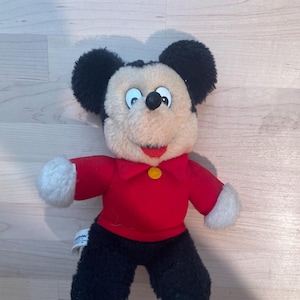 Puede incluir: Un peluche vintage de Mickey Mouse. El peluche presenta una camisa roja con un bot&oacute;n amarillo, pantalones negros y guantes blancos. La cara de Mickey es de color crema con orejas negras y una nariz negra. Un cl&aacute;sico de Disney.