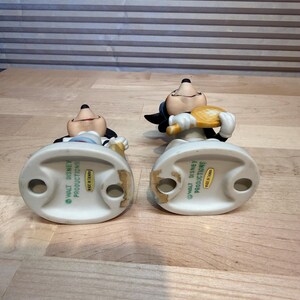 Puede incluir: Dos figuras vintage de Mickey Mouse. Una sostiene una raqueta de tenis, la otra una pelota de tenis. Ambos llevan guantes blancos, pantalones cortos negros y tienen una expresi&oacute;n sonriente. Las figuras son de cer&aacute;mica y miden unos 10 cm de alto.