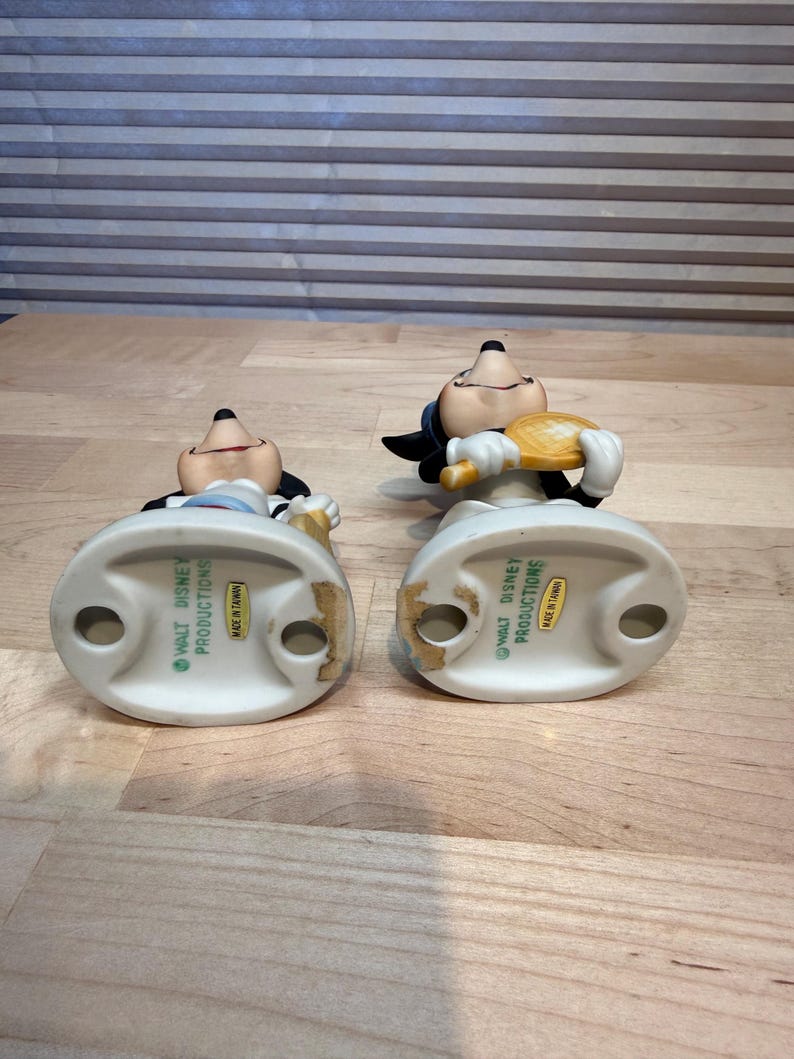 Puede incluir: Dos figuras vintage de Mickey Mouse. Una sostiene una raqueta de tenis, la otra una pelota de tenis. Ambos llevan guantes blancos, pantalones cortos negros y tienen una expresi&oacute;n sonriente. Las figuras son de cer&aacute;mica y miden unos 10 cm de alto.