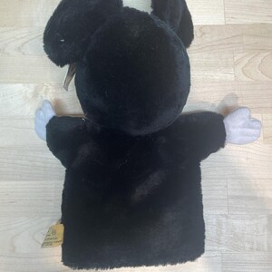 May include: A black plush Mickey Mouse hand puppet with white gloves and a tag. The puppet has large ears and is made of soft, fuzzy material. The puppet's arms are outstretched.