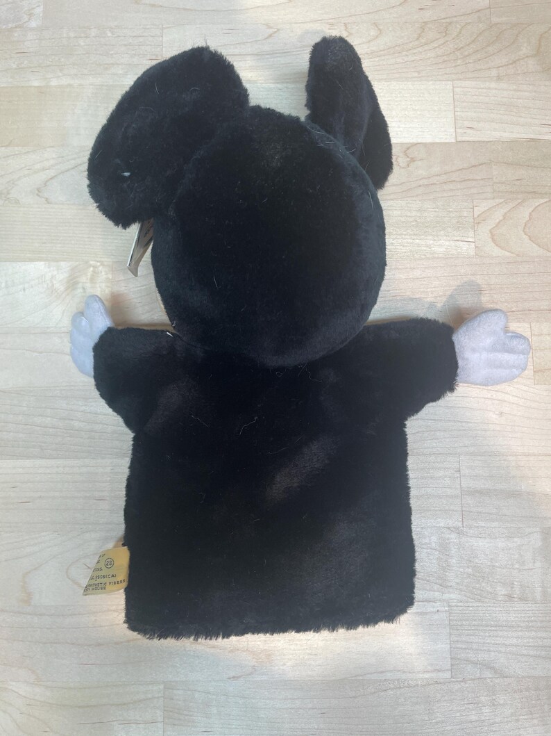 May include: A black plush Mickey Mouse hand puppet with white gloves and a tag. The puppet has large ears and is made of soft, fuzzy material. The puppet's arms are outstretched.
