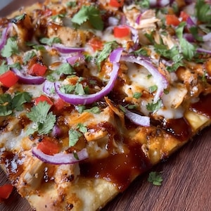 May include: A flatbread pizza with toppings including chicken, red onion, diced tomatoes, and cilantro. The pizza is drizzled with a dark sauce and sits on a wooden surface. The crust is golden brown.