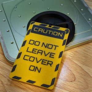 Op de afbeelding: Een geel waarschuwingsbord met zwarte tekst met de tekst "CAUTION DO NOT LEAVE COVER ON".