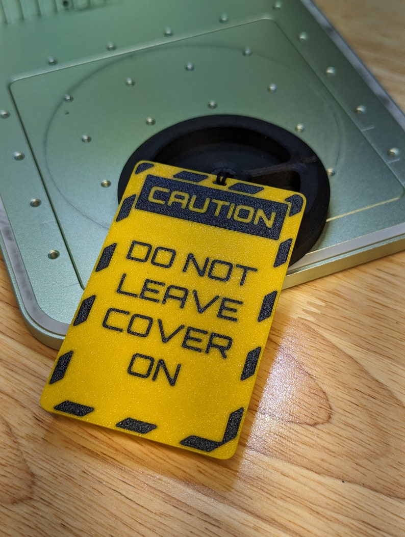 Op de afbeelding: Een geel waarschuwingsbord met zwarte tekst met de tekst "CAUTION DO NOT LEAVE COVER ON".