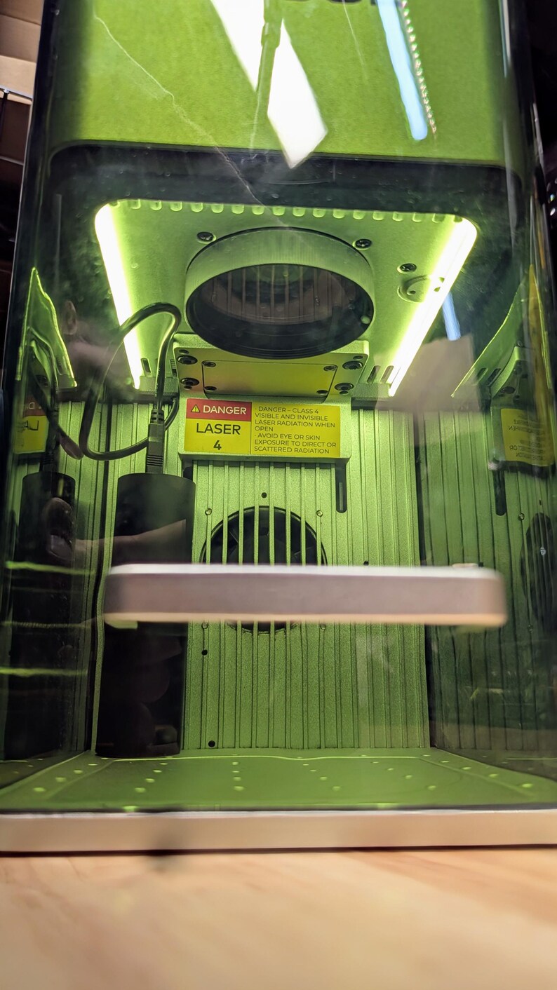 May include: A green laser engraving machine with a warning sign that reads "Danger Class 4 Laser - Avoid eye or skin exposure to direct or scattered radiation".