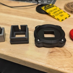 Op de afbeelding: Vier verschillende zwarte kunststof onderdelen voor een aangepast mechanisch toetsenbord, waaronder een toetsdop, een schakelaarplaat, een plaatbevestiging en een toetsdoppenhouder. Een rode knop met het woord "FIRE" is ook te zien.