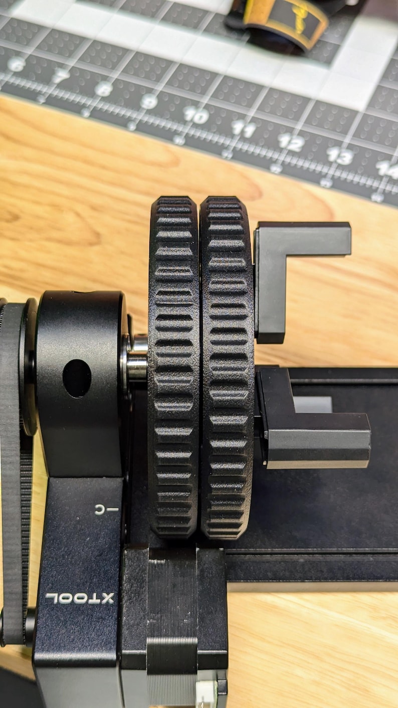 K&ouml;nnte beinhalten: Nahaufnahme eines schwarzen 3D-Druckers mit zwei schwarzen Zahnr&auml;dern und einem schwarzen Arm. Der Drucker hat ein Etikett mit der Aufschrift "XTOOL" und "C-."
