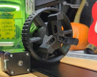 May include: A black 3D printed wheel with a three-pronged, black, metal center. The wheel has a textured, black, rubber tire.