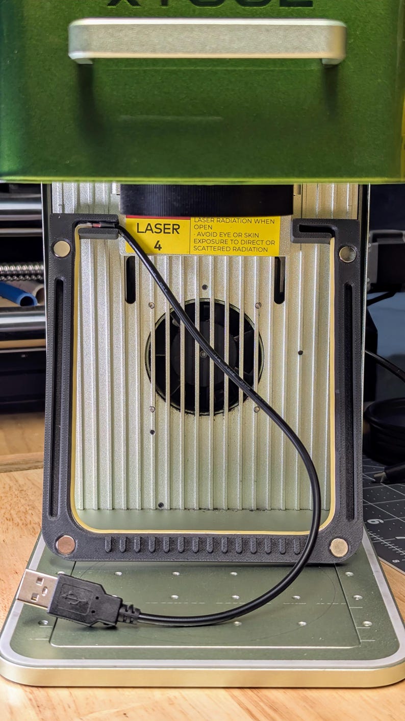 May include: Close-up of a laser engraver with a warning label that reads "LASER RADIATION WHEN OPEN AVOID EYE OR SKIN EXPOSURE TO DIRECT OR SCATTERED RADIATION". The laser is labeled "LASER 4".