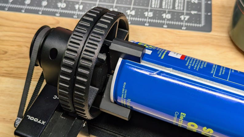 K&ouml;nnte beinhalten: Eine schwarze und silberne Dosenrolle mit einer blauen Dose, die eingesetzt ist. Die Rolle hat einen schwarzen Riemen und ein schwarzes Zahnrad. Die Dose ist mit "Super Oil Electric Contact Cleaner" beschriftet.