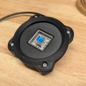 Op de afbeelding: Een zwarte ronde mechanische toetsenbord-toetsdop met een blauwe toetsdop en een transparante schakelaar.